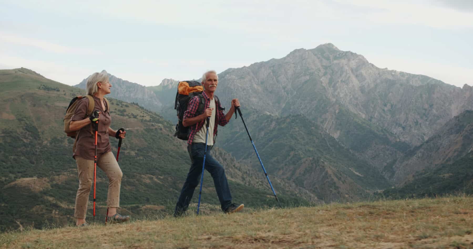 Active,Senior,Caucasian,Couple,Hiking,In,Mountains,With,Backpacks,,Enjoying
